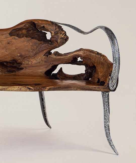 Eine Seitenansicht einer einzigartigen Teakholz-Bank mit geschwungenen, metallischen Beinen und einer charakteristischen, natürlich geformten Holzoberfläche, die durch Hohlräume und natürliche Holzmaserung akzentuiert wird