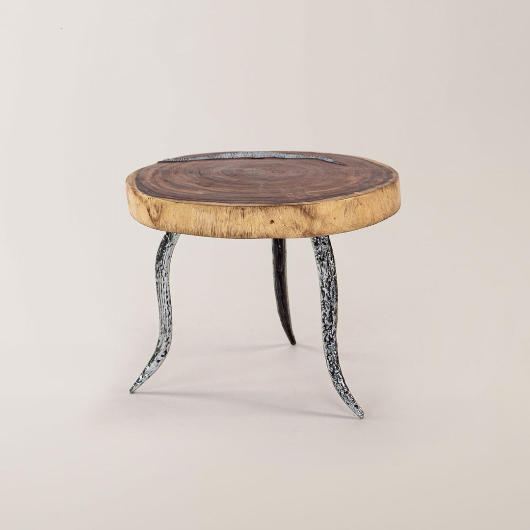 Runder Beistelltisch aus der SuarMetallic Harmony Kollektion, gekennzeichnet durch eine natürliche Holzoberfläche mit deutlich sichtbarer Maserung und elegante, geschwungene Metallbeine mit detailreicher Musterung, perfekt für moderne Innenräume.