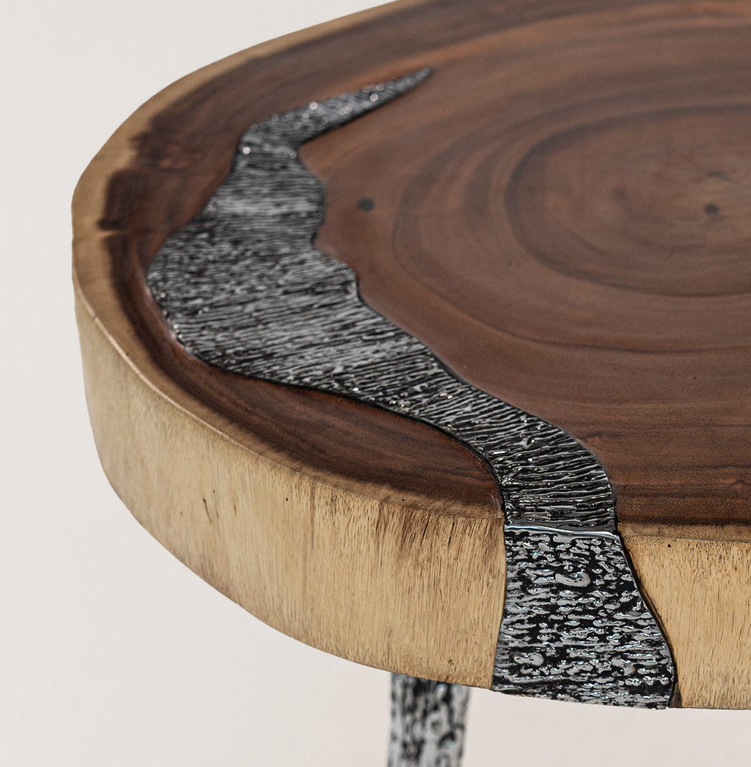 Nahaufnahme eines SuarMetallic Harmony Beistelltisches, der eine einzigartige Verbindung aus natürlicher Holzplatte und eingebetteten metallischen Details zeigt, getragen von kunstvoll gemusterten Metallbeinen, die ein modernes und elegantes Design betonen.