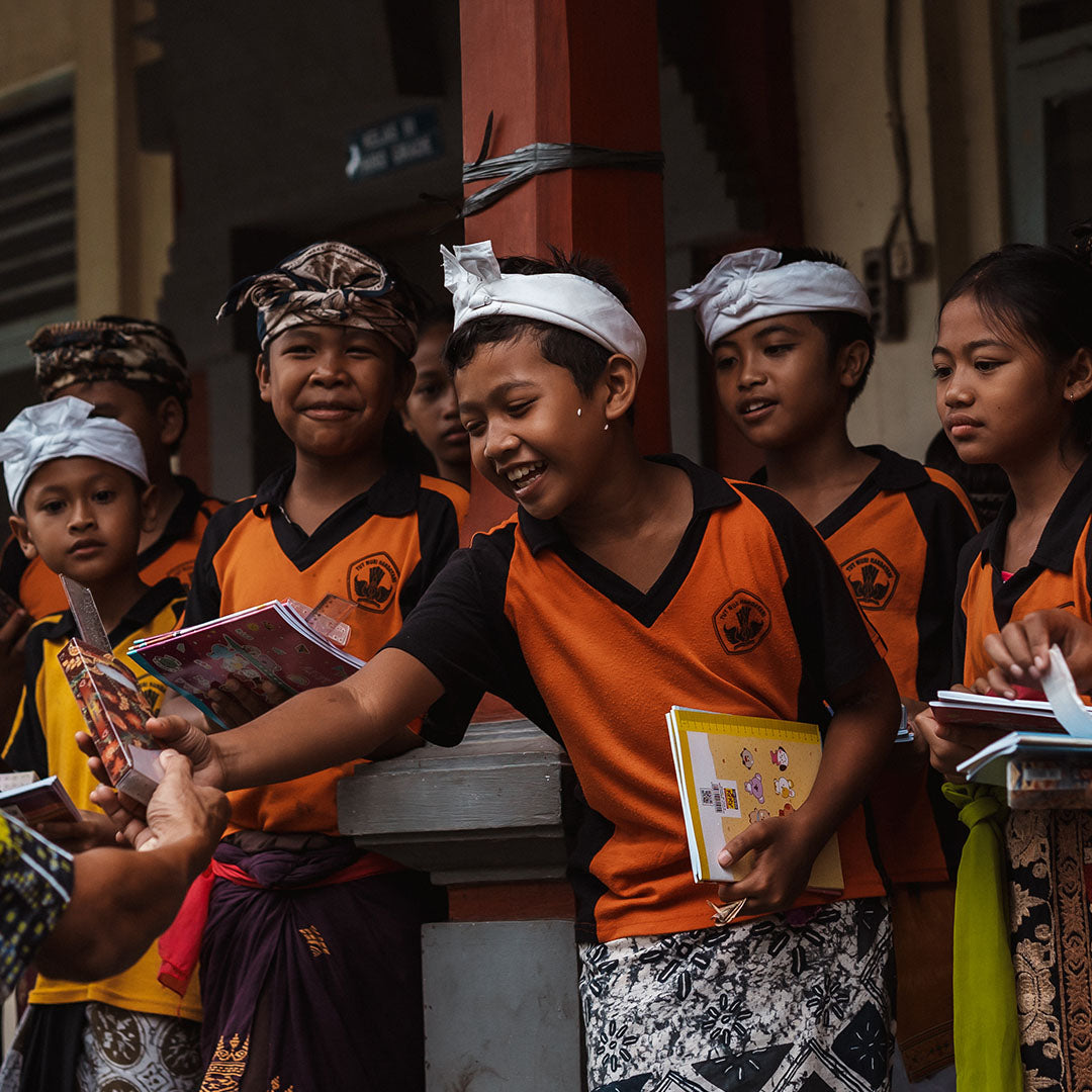 INDOO unterstützt lokale Schule in Indonesien: Schülerinnen und Schüler in traditionellen Gewändern lächeln und halten Bücher in den Händen, gefördert durch die Unterstützung von INDOO.